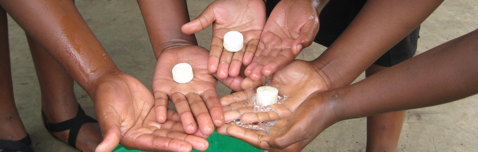 image of three sets of hands with soap cakes and water basin to illustrate the water and sanitation work done by the uphill trust