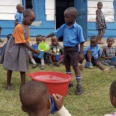 Kindergarten children in Uganda receiving a cup of porridge from the Uphill Porridge Club